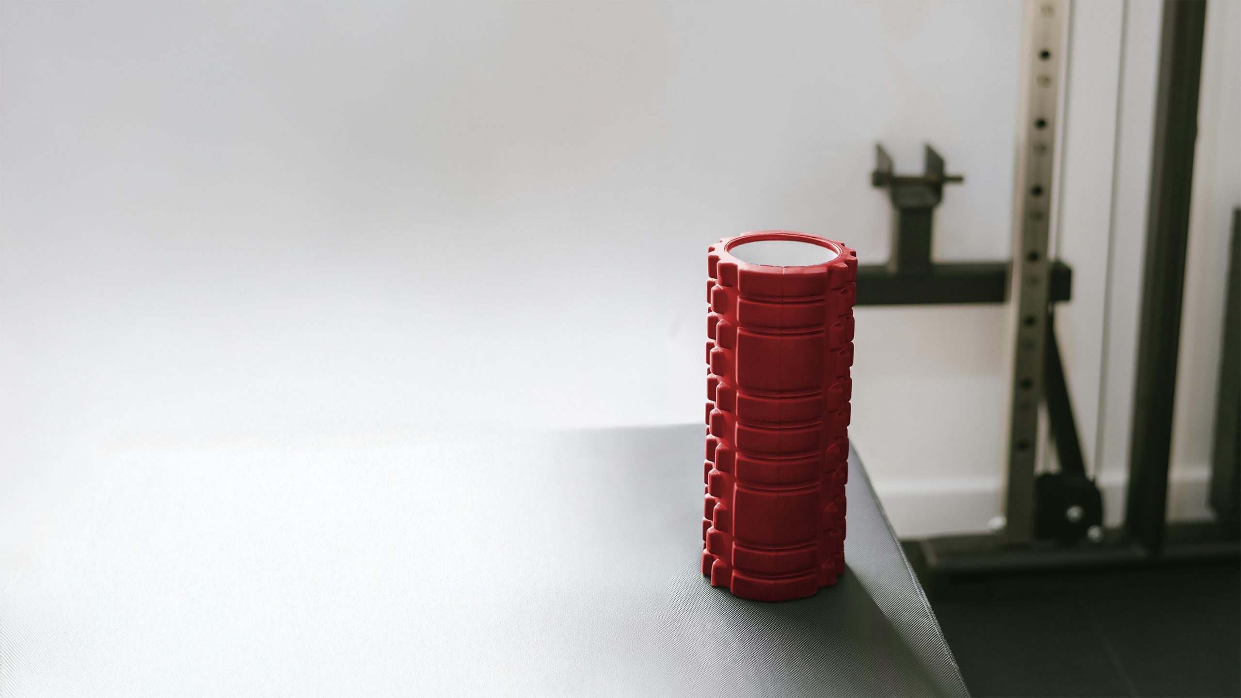 A red foam roller sitting on a therapy bench.