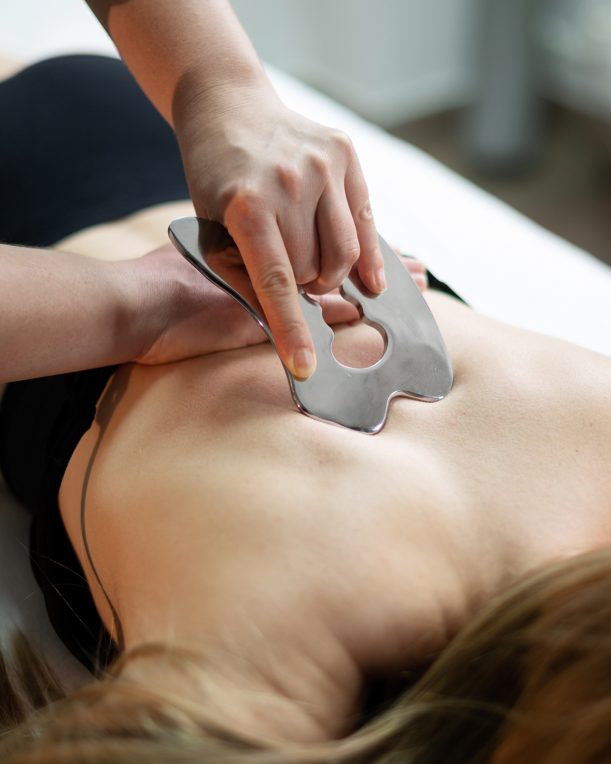 A woman lying on a table while a physical therapist uses an instrument on her back. 