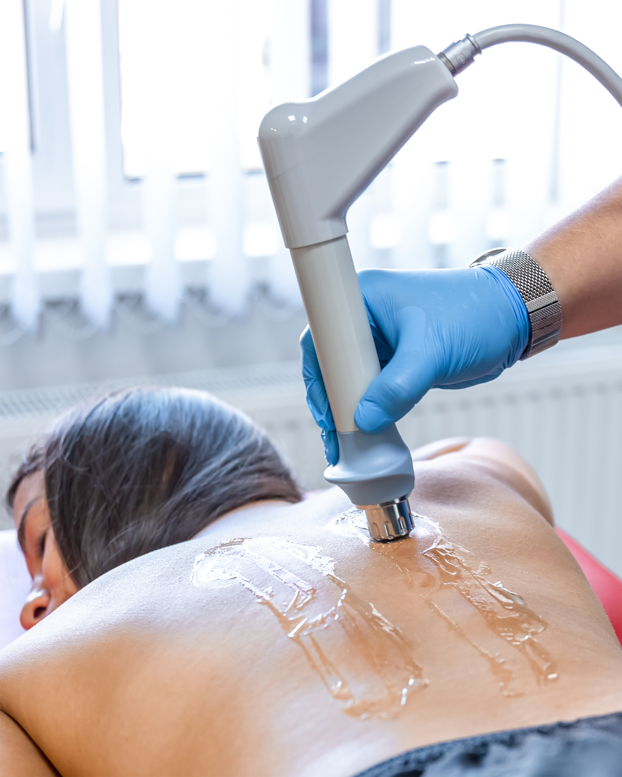 A woman lying on a table with gel on her back being treated with a radial therapy gun. 