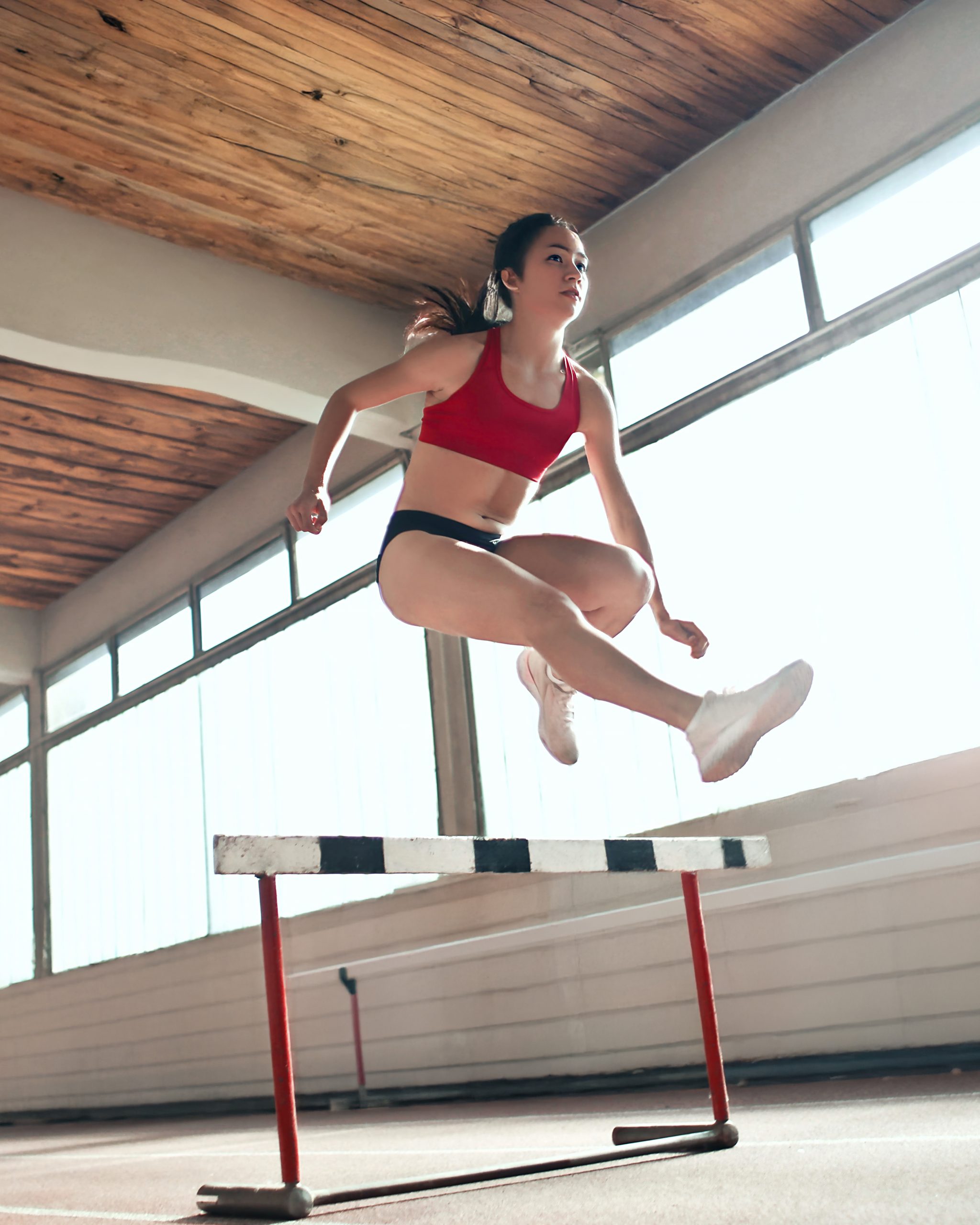 A young woman jumping over a hurdle.
