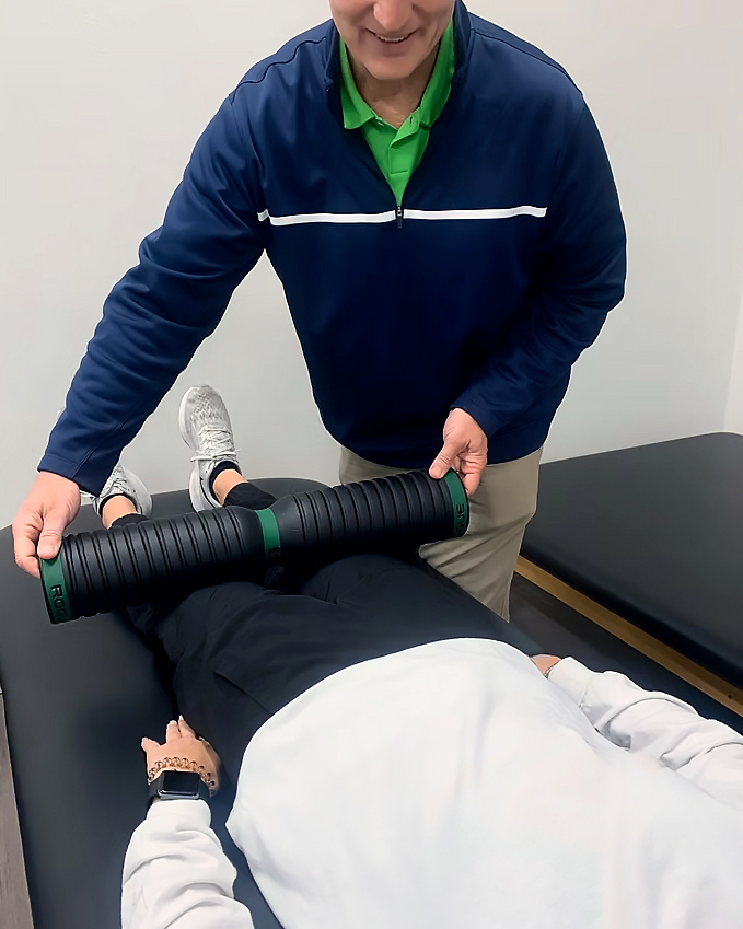 A physical therapist rolling a foam roller over a patients legs. 