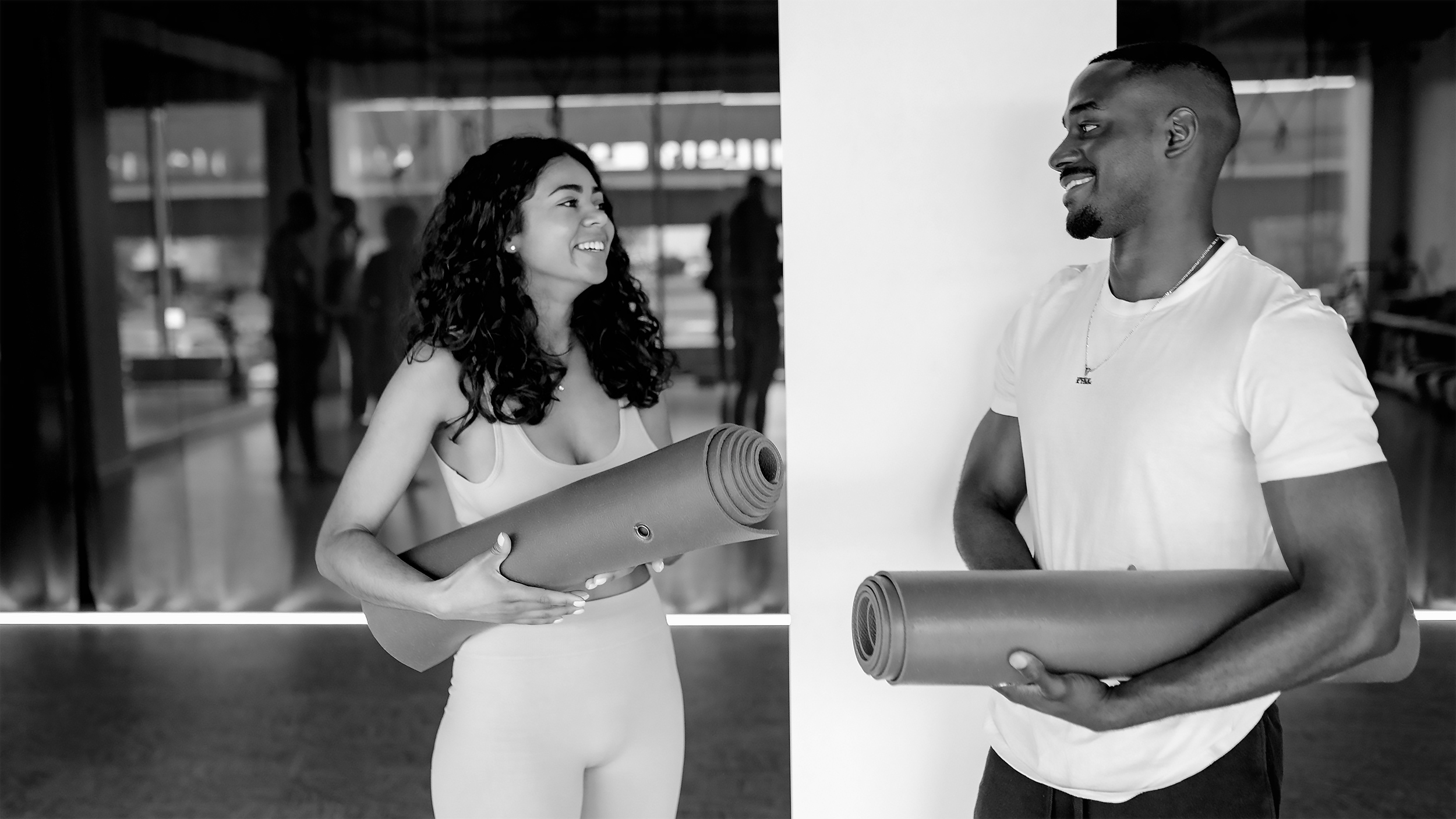 A man and a woman holding yoga mats and smiling.
