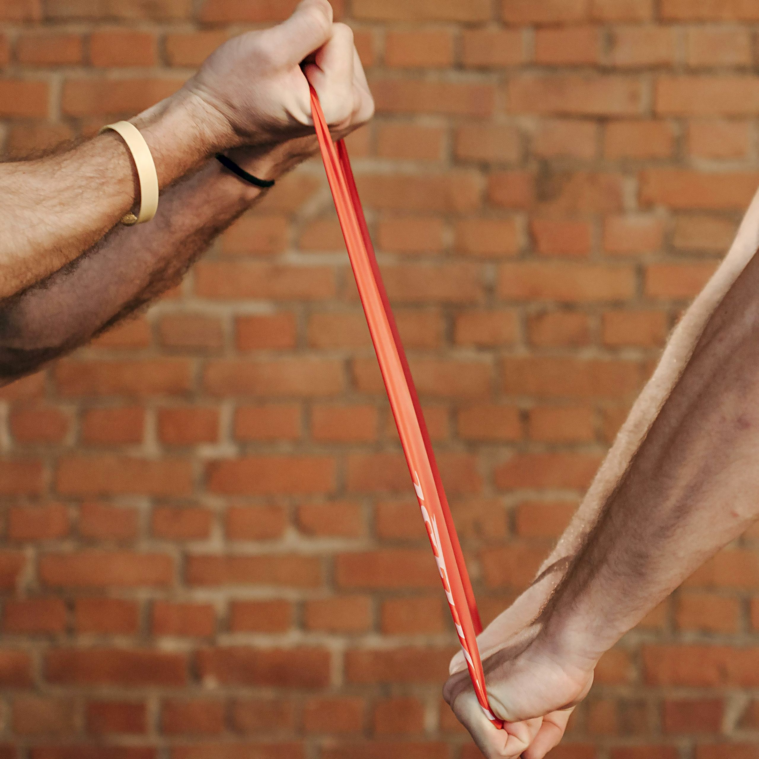 Two sets of hands pulling a resistance band in opposite directions.