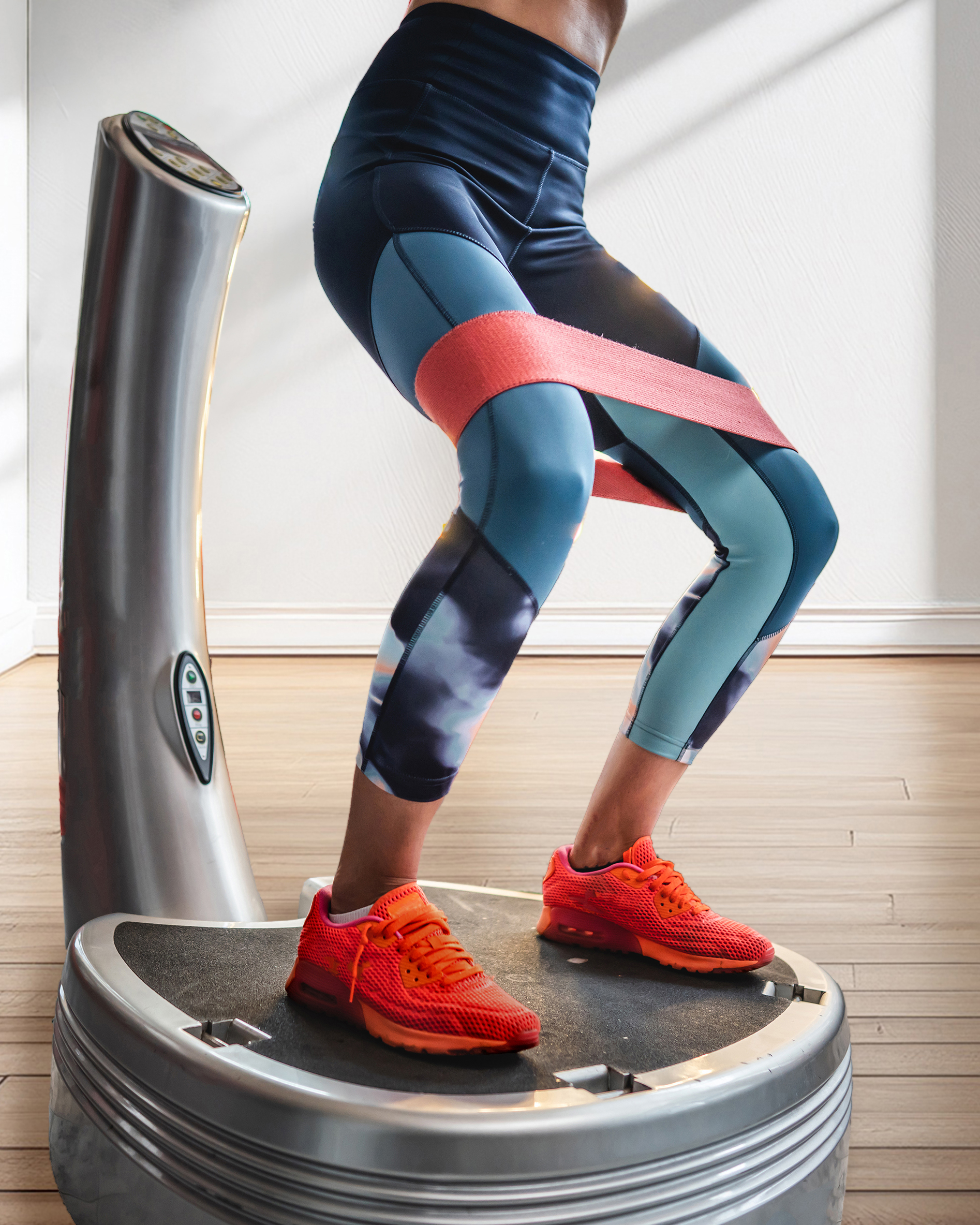 A woman standing on a vibration plate with an exercise band around her knees.